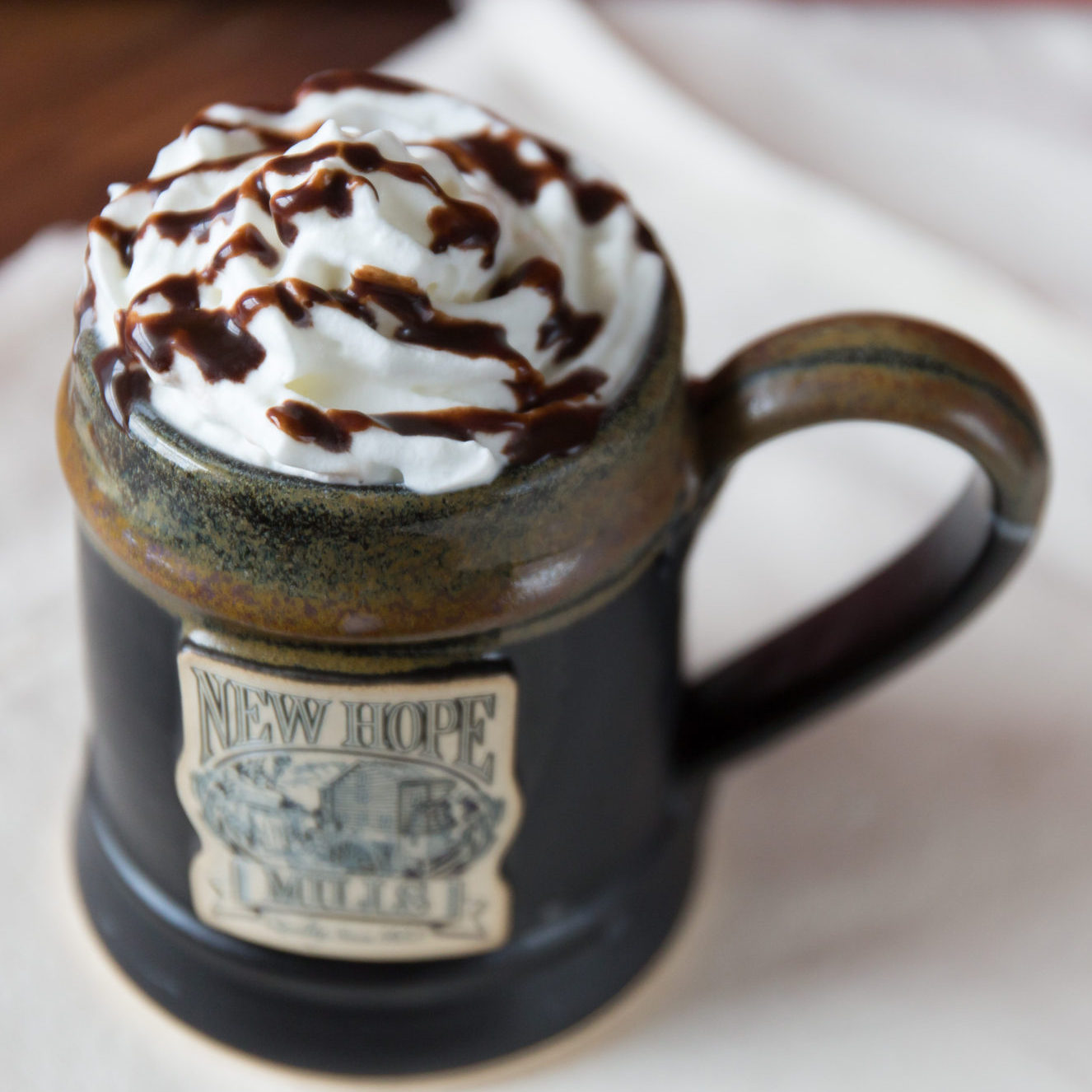 Photo of drink with whipped cream and 100部啪啪视频 syrup drizzle in a black pottery mug