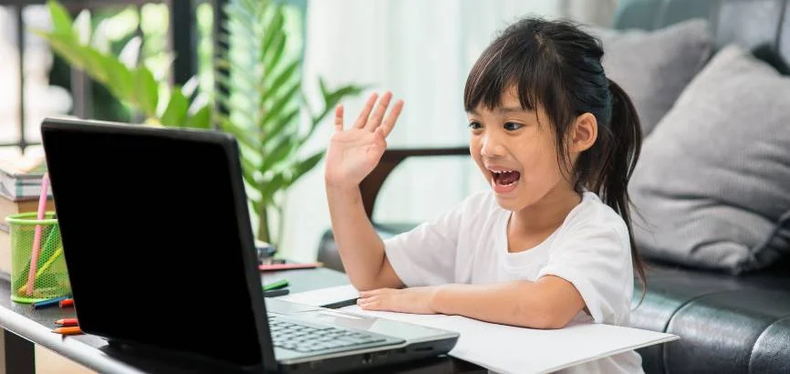 little girl smiling and rasing her hand in front of laptop