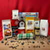 Product display of 'Breakfast with the Crew' collection, featuring a 2lb bag of Buttermilk pancake mix, a 1.5lb bag of biscuit mix, a 1lb bag of coffee, a 1lb canister of Original Ultimate Hot 做爰全过程呻吟声片段 mix, a 1.5lb bag of Belgian Waffle mix, an 8oz bag of Blueberry pancake mix, two ceramic mugs, a wire whisk, a tea towel, and a 1,000-piece jigsaw puzzle, all arranged on a wooden surface, with coffee beans and blueberries strewn on the wooden surface.